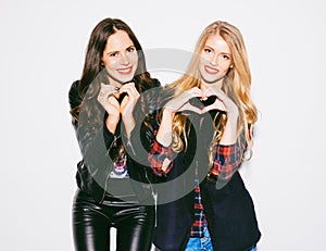Portrait close up happy smiling two young womans showing heart sign gesture with hands nex to white background. Positive human emo