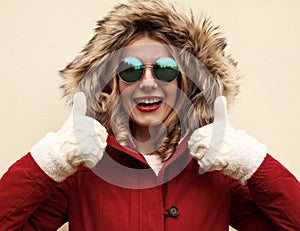 Portrait close up happy smiling woman showing thumbs up as like sign wearing red jacket with fur hood and white mittens