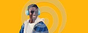 Portrait close up of happy smiling young african man in wireless headphones listening to music looking away isolated on yellow