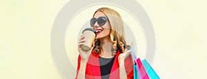 Portrait close up happy smiling young woman with colorful shopping bags and coffee cup wearing a red business blazer on