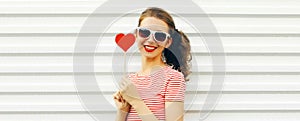 Portrait close up happy smiling young woman with red sweet heart shaped lollipop and ponytail hairstyle on white background