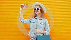 Portrait close up of happy smiling young woman taking selfie picture by smartphone with shopping bags wearing straw hat over an