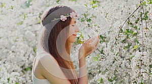 Portrait close up lovely young woman touching petals of flowers wearing a floral headband in a spring blooming garden