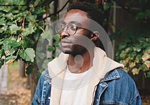 Portrait close-up modern african man thinking and looking away wearing eyeglasses in autumn city park on background