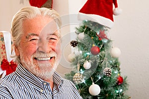 Portrait and close up of old mature man smiling and laughing looking at the camera with a christmas tree at the background - old