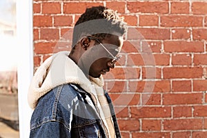 Portrait close up side view stylish african man wearing sunglasses and jeans jacket with hood on city street