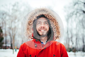 Portrait, close-up of a young stylishly dressed man smiling with a beard dressed in a red winter jacket with a hood and fur on his