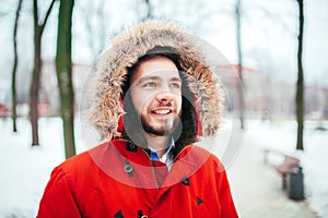 Portrait, close-up of a young stylishly dressed man smiling with a beard dressed in a red winter jacket with a hood and fur on his