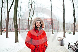 Portrait, close-up of a young stylishly dressed man smiling with a beard dressed in a red winter jacket with a hood and fur on his photo