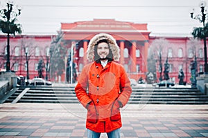 Portrait, close-up of a young stylishly dressed man smiling with a beard dressed in a red winter jacket with a hood and fur on his photo