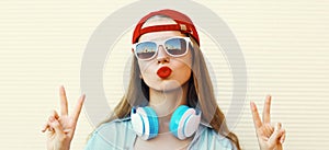 Portrait close up of young woman in red baseball cap and wireless headphones listening to music over white background