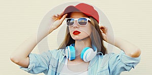 Portrait close up of young woman in red baseball cap and wireless headphones listening to music over white background