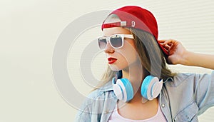 Portrait close up of young woman in red baseball cap and wireless headphones listening to music over white background