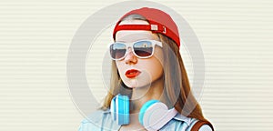 Portrait close up of young woman in red baseball cap and wireless headphones listening to music over white background