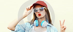 Portrait close up of young woman in red baseball cap and wireless headphones listening to music over white background