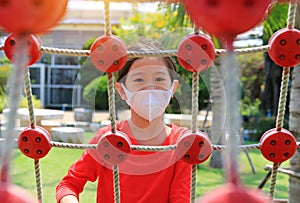 Portrait closeup asian little girl wearing protective mask while playing on climbing rope net