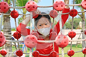 Portrait closeup asian little girl wearing protective mask while playing on climbing rope net