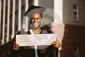 Portrait closeup of black guy standing with cardboard poster on street in sunny day looking for job, selective focus