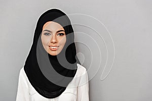 Portrait closeup of muslim prayer woman 20s in religious headscarf smiling and looking at camera, isolated over gray background