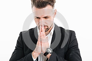 Portrait closeup of serious concentrated man wearing black jacket putting palms together for praying, isolated over white