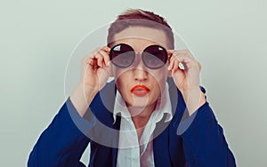 Portrait closeup Surprised young woman in round shaped sunglasses over green gray background. Angry girl business blue navy suit,