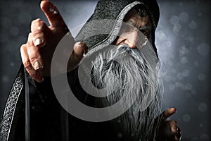 Portrait closeup of a wise Warlock old hooded wizard posing ready to cast an enchanted powerful spell .