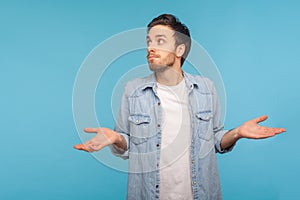Portrait of clueless confused man in worker denim shirt shrugging shoulders as doesn`t know answer