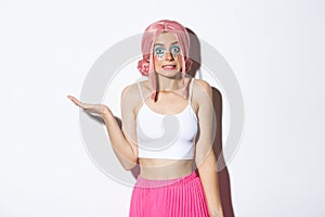Portrait of clueless cute girl in pink wig shrugging, looking unaware, standing in halloween costume with bright makeup