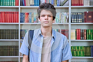 Portrait of college student guy with backpack looking at camera inside library of educational building