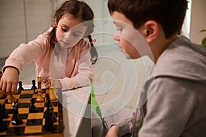 Portrait of a concentrated 4 years old little girl picking up a chess piece while making move on chess board, playing with her