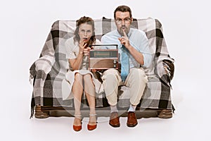 Portrait of concentrated couple, man and woman sitting on sofa and listening to the news on radio