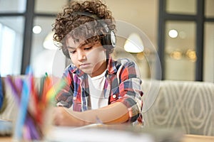 Portrait of concentrated hispanic school boy wearing headphones, preparing homework while sitting at the desk at home