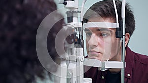 Portrait of concentrated man sitting at retina camera as woman checking back of the eye. Focused serious Caucasian