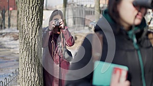 Portrait of concentrated serious woman taking photos peeping after lady with binoculars in winter park. Focused