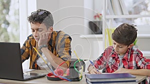 Portrait of concentrated teen and little students doing homework indoors sitting at table. Focused schoolboy writing in