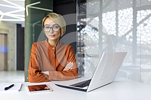 Portrait of concentrated thinking and serious woman at workplace inside office, businesswoman with crossed arms sitting