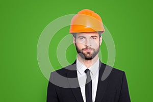 Portrait of concentrated, thoughtful architector with stubble in orange safety helmet, hardhat and black tux with tie