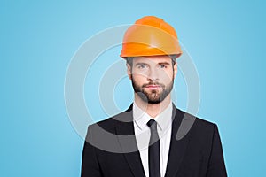 Portrait of concentrated, thoughtful architector with stubble in orange safety helmet, hardhat and black tux with tie