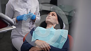 Portrait of concentrated woman in dental chair looking up listening to professional doctor talking. Beautiful patient