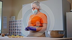 Portrait of concentrated woman in face mask making dumplings with potato balls placing food on flour on table. Medium