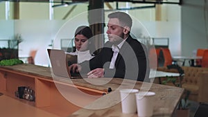 Portrait of concentrated young woman surfing Internet on tablet as focused man joining colleague at office bar and