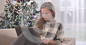 Portrait of concentrated young woman using laptop on Christmas weekends. Beautiful brunette Caucasian lady resting on