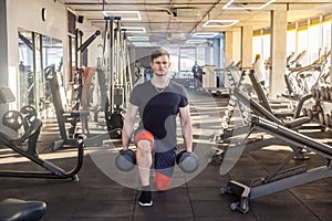 Portrait of concentration young adult man handsome athlete working out in gym, standing on the knees and holding two dumbbells,