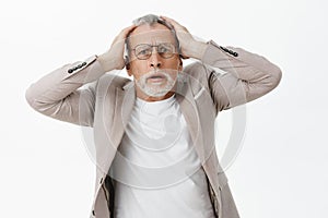 Portrait of concerned and troubled shocked senior man with white hair and beard in suit and glasses holding hands on