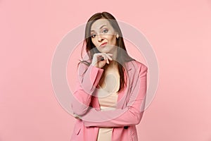 Portrait of concerned young woman wearing jacket put hand prop up on chin looking camera  on pastel pink