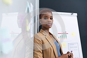 Portrait of confident african american young businesswoman leaning on whiteboard in board room