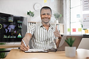 Portrait of confident african businessman in stylish formal wear writing notes using laptop