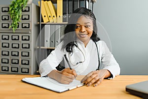 Portrait confident African female doctor medical professional writing patient notes isolated on hospital clinic hallway