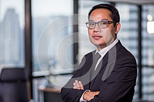 Portrait of confident asian business man in eyeglasses standing in offiec looking at camera