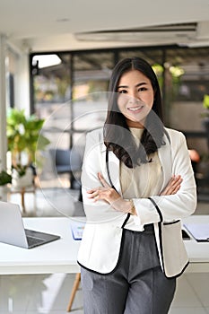 Portrait of a confident Asian businesswoman stands with arms crossed in the office